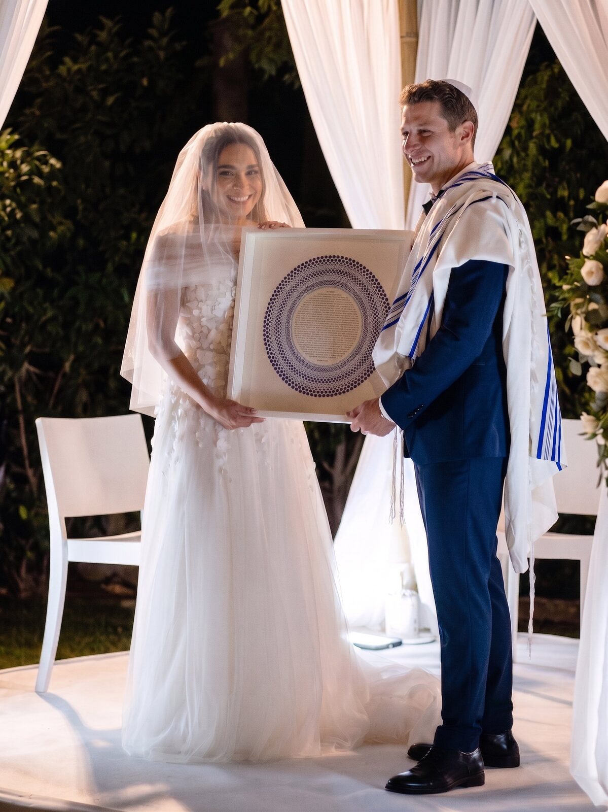 The couple holding their custom blue-dots ketubah under the chuppah on their wedding day